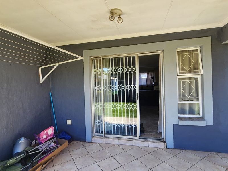 A covered patio area featuring tiled flooring, a sliding glass door with security gate, and a wall-mounted drying rack.