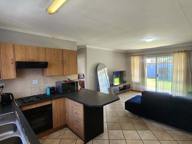 Open-plan kitchen and living area featuring wood-finish cabinetry, tiled flooring, and direct access to the rear garden through a sliding glass door.