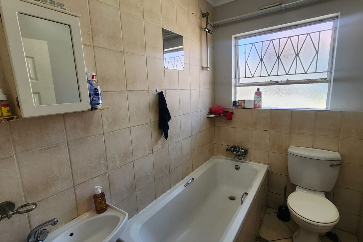 A functional bathroom featuring a bathtub with shower head, wall-mounted basin, and toilet, finished with tiled walls and a window with security bars.
