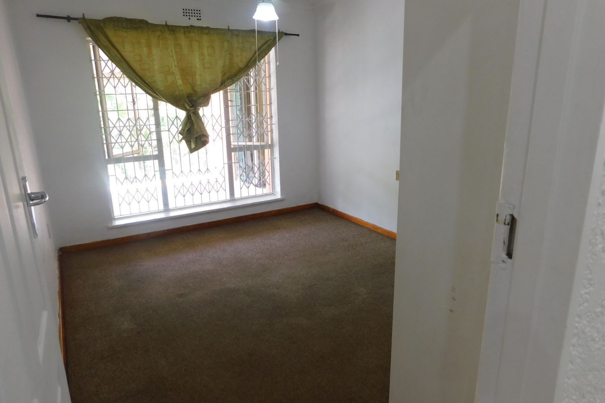 An empty bedroom featuring carpeted flooring, a ceiling fan, and a window fitted with a security gate.