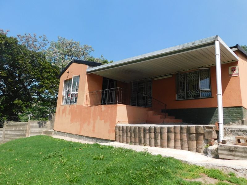 Rear exterior view of the house featuring a covered patio area, concrete retaining wall, and metal security gates on windows and doors.