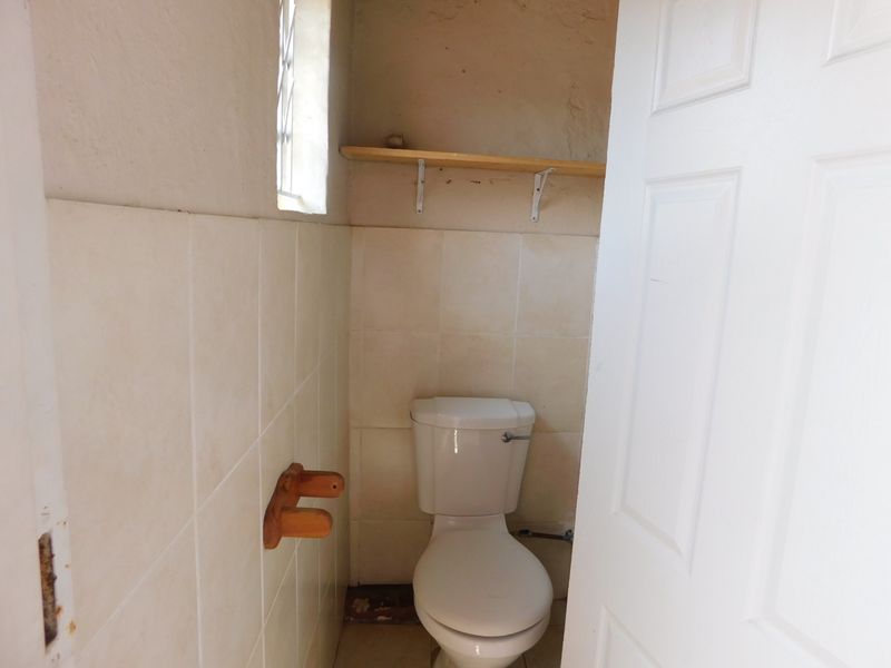 A small, dated guest toilet featuring wall tiling, a built-in shelf, and a leaded glass window, currently in need of cosmetic refurbishment.