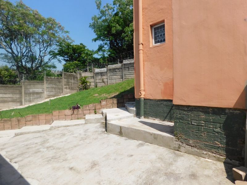 Rear exterior area featuring concrete paving, a retaining wall, and a precast boundary fence with security razor wire.
