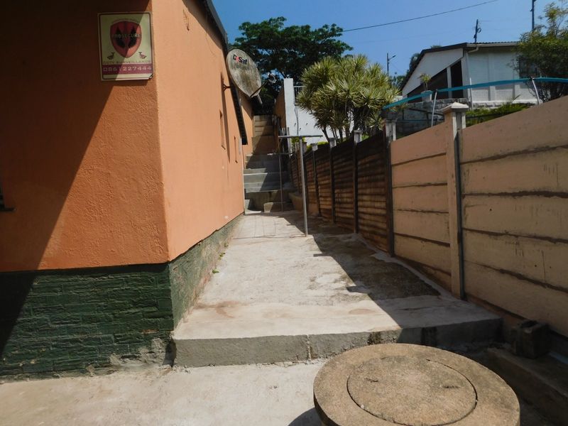 A narrow exterior side passage featuring concrete paving, stairs, and a precast boundary wall, showing signs of weathering and wear.