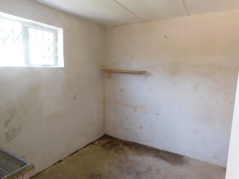 A vacant utility space featuring concrete flooring, security bars on the window, and a wall-mounted shelf, requiring cosmetic refurbishment.
