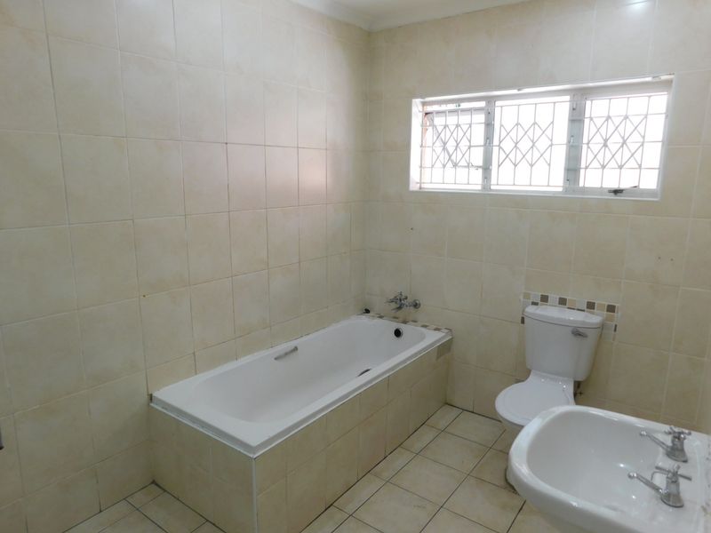 A functional bathroom featuring a built-in bathtub, pedestal basin, and toilet, finished with neutral ceramic wall and floor tiles.
