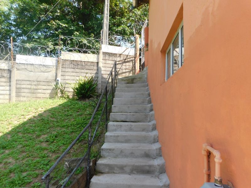 Exterior rear view showing a concrete staircase with metal handrail leading up alongside the building, featuring a perimeter wall with security razor wire.
