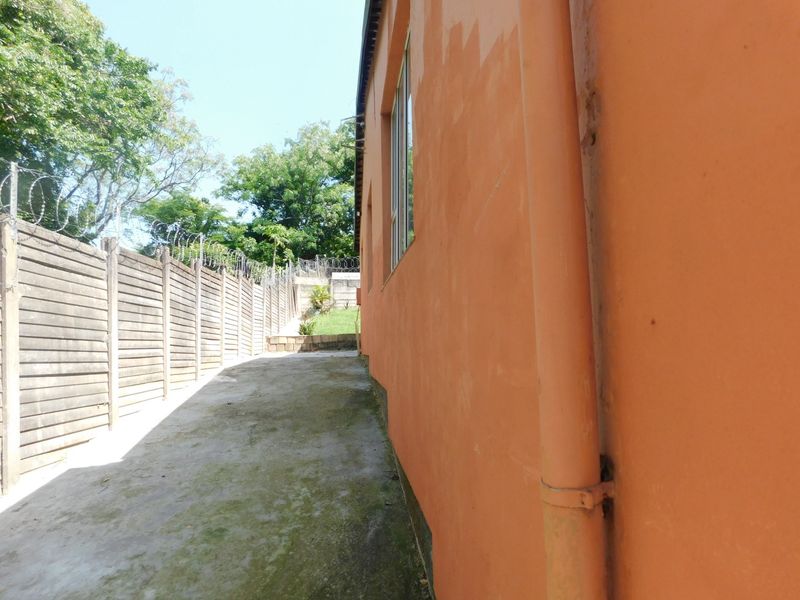 Side exterior view of the property featuring a concrete paved walkway, precast boundary wall with razor wire, and exterior wall drainage pipe.