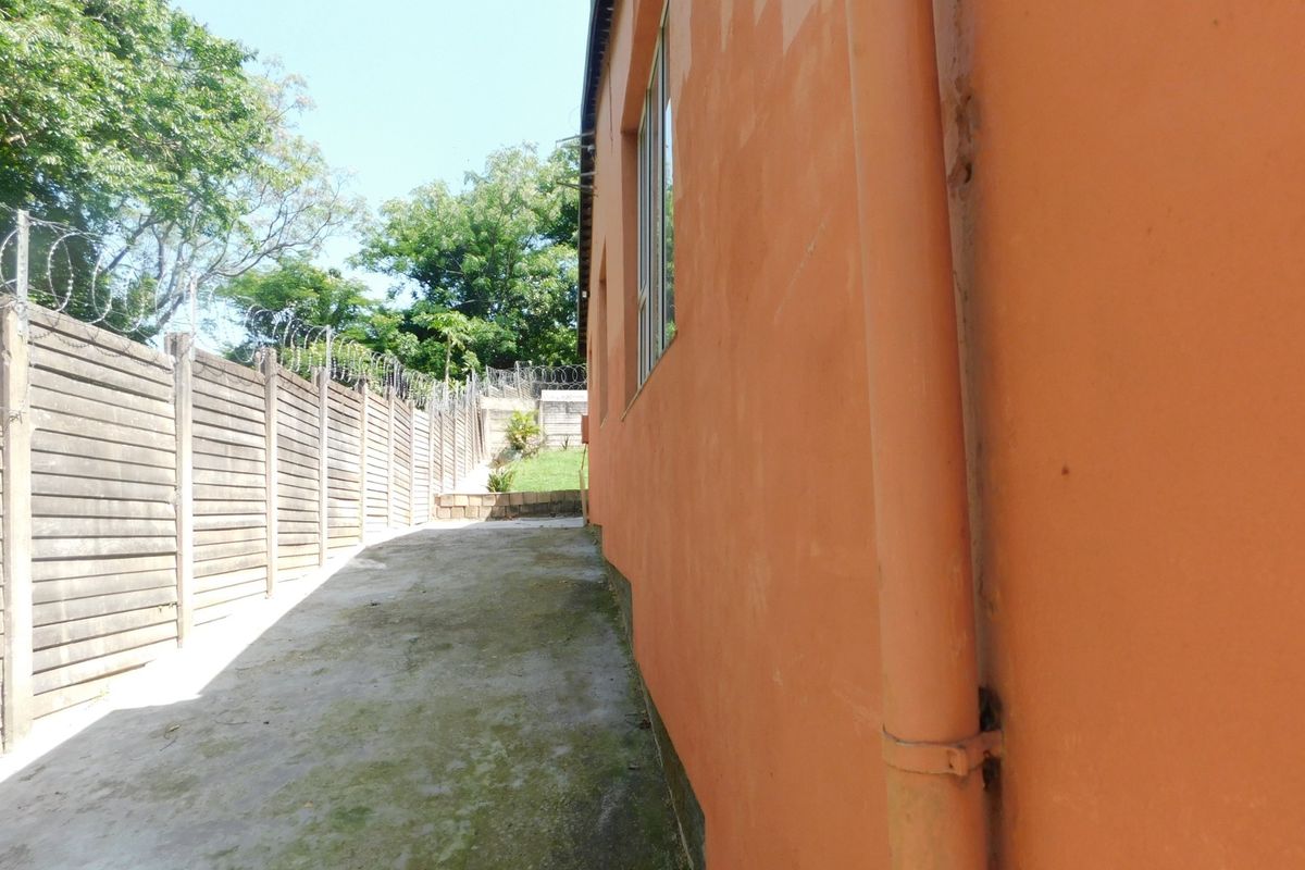 Side exterior view of the property featuring a concrete paved walkway, precast boundary wall with razor wire, and exterior wall drainage pipe.