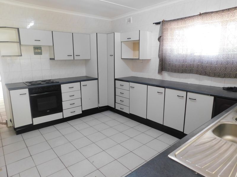 A functional kitchen featuring white built-in cabinetry, dark laminate countertops, a built-in oven with hob, and tiled flooring throughout.