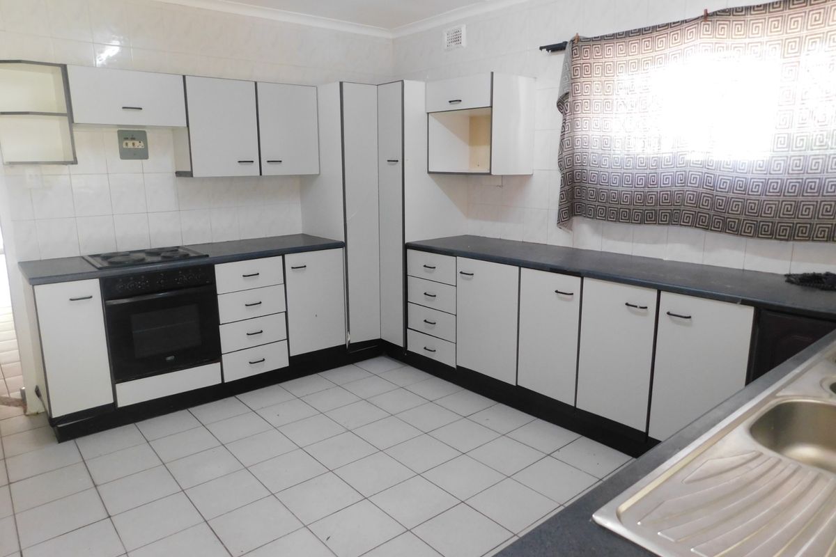 A functional kitchen featuring white built-in cabinetry, dark laminate countertops, a built-in oven with hob, and tiled flooring throughout.