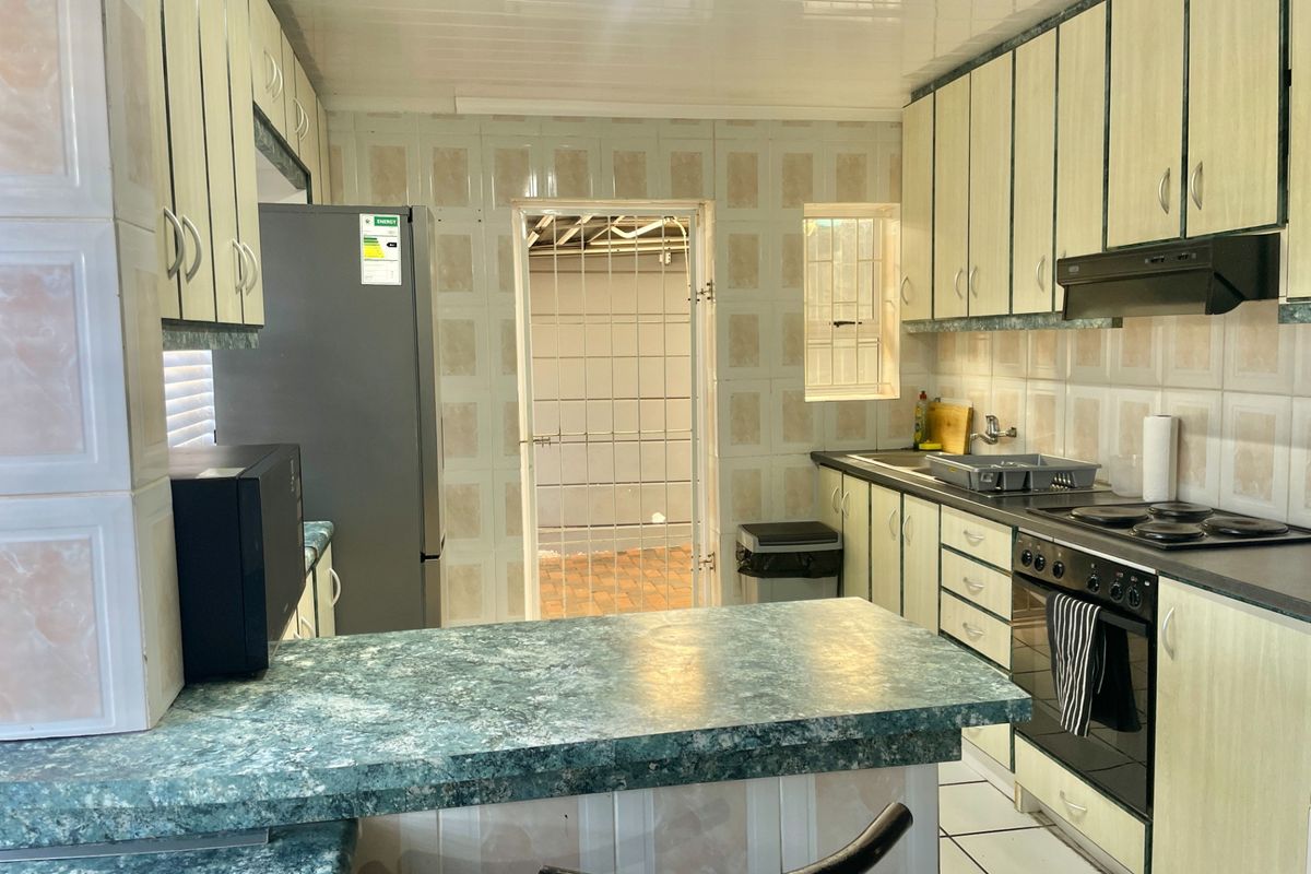 Functional kitchen featuring laminate cabinetry, built-in oven with hob, extractor fan, and tiled splashbacks, with direct access to an exterior area via a security gate.