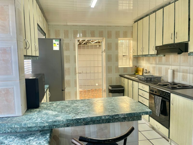 Functional kitchen featuring laminate cabinetry, built-in oven with hob, extractor fan, and tiled splashbacks, with direct access to an exterior area via a security gate.