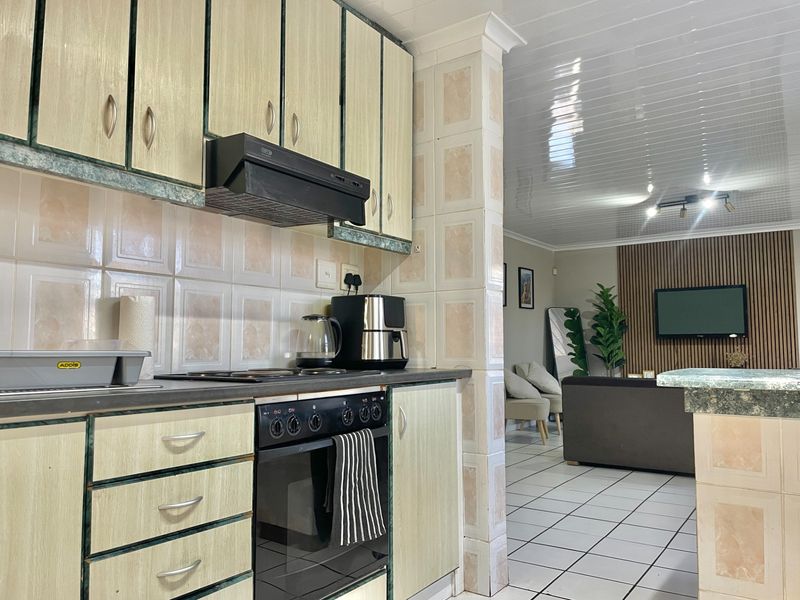 Open-plan kitchen and living area featuring built-in cabinetry, integrated oven and hob, tiled backsplash, and tiled flooring throughout.