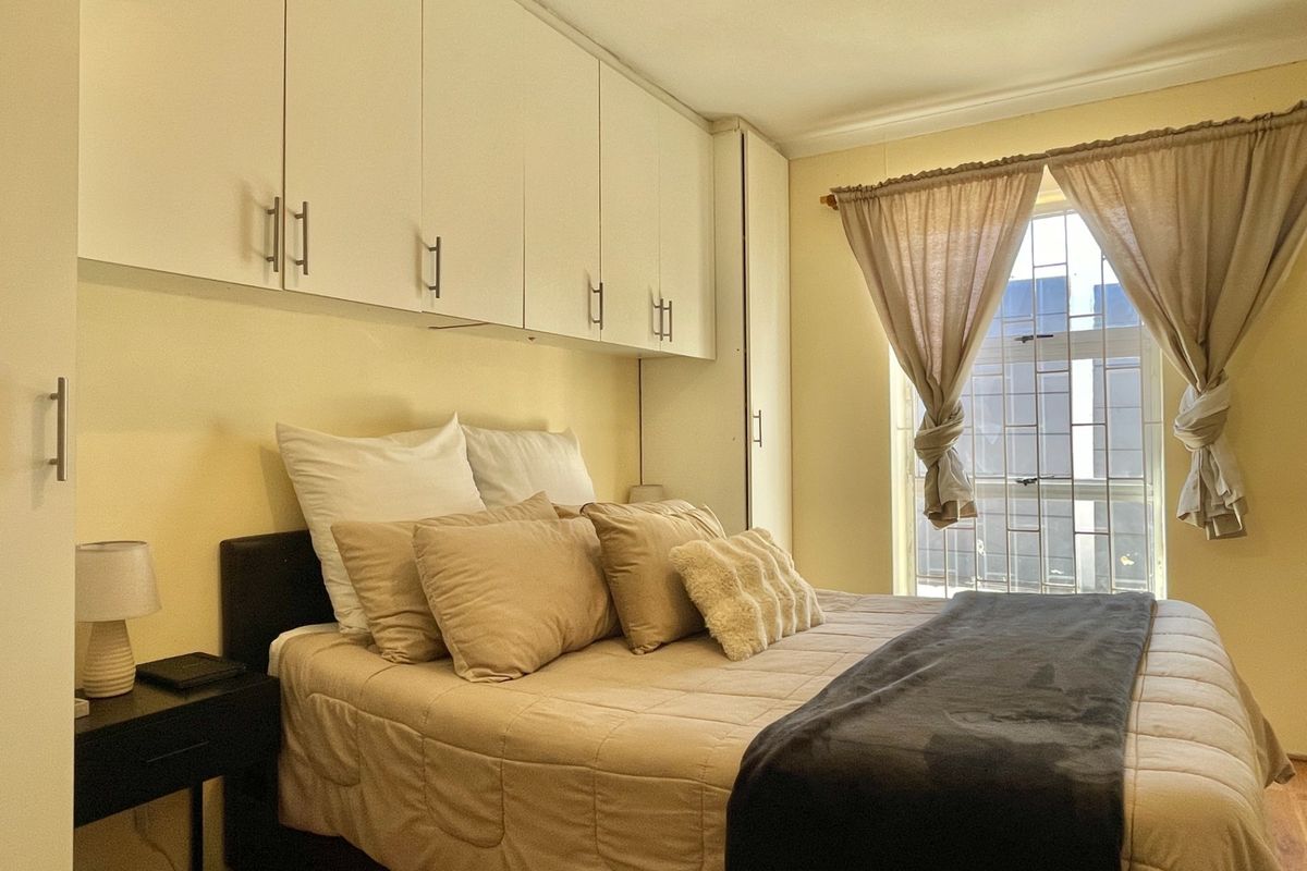 A bedroom featuring built-in cupboards and a window fitted with security bars, offering a functional and well-utilized living space.