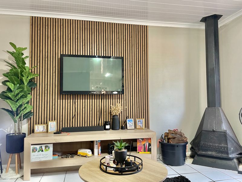 A cozy living room featuring a modern slatted wood feature wall, a black metal fireplace, and neutral tiled flooring.