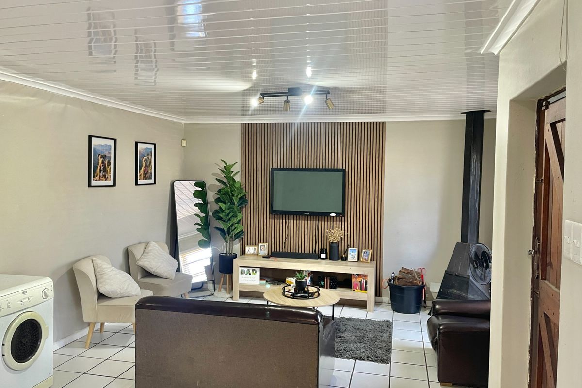 A comfortable living room featuring a modern wood-slat accent wall, a built-in fireplace, tiled flooring, and a clean PVC ceiling finish.