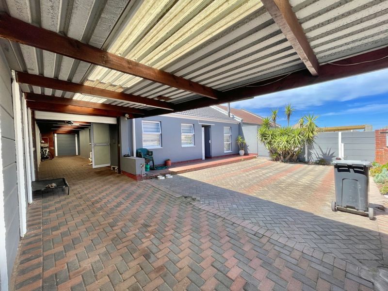 A spacious rear exterior area featuring a covered patio with timber beams, paved driveway, and a secure boundary wall.