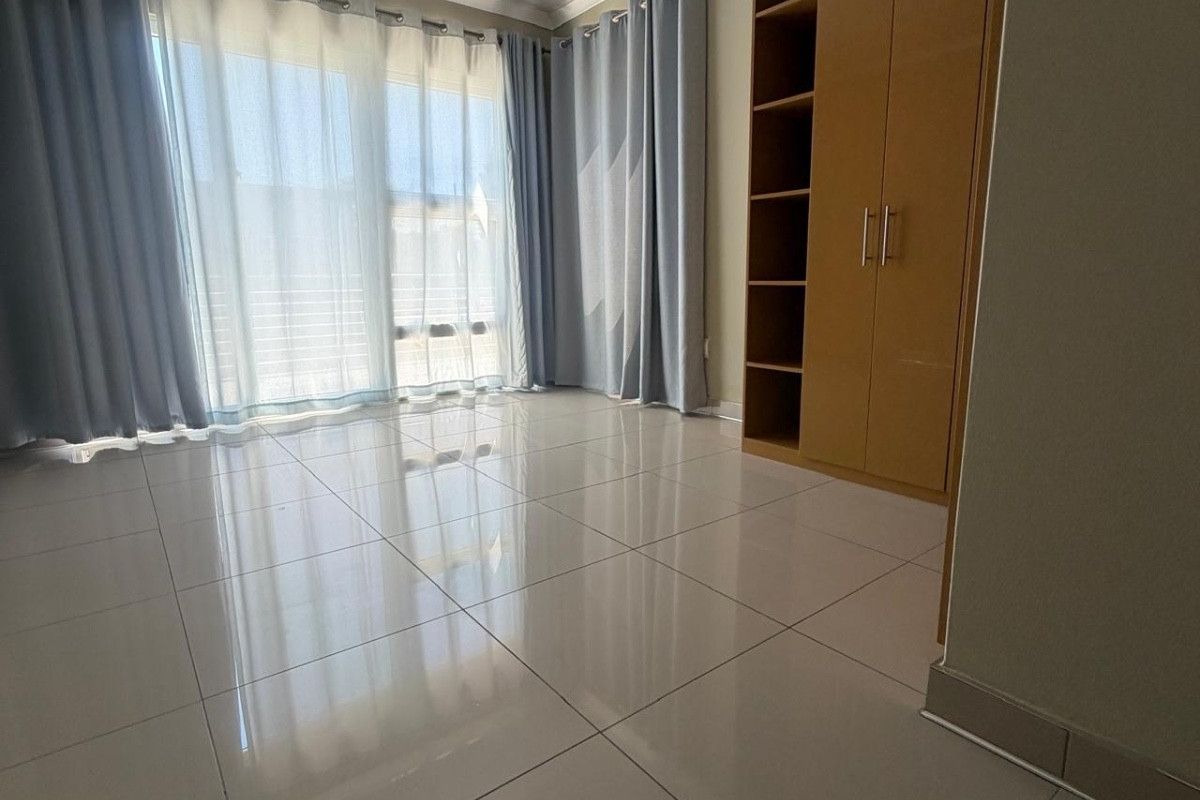 A bright, empty bedroom featuring polished tiled flooring, built-in wooden cupboards, and large sliding glass doors providing ample natural light.