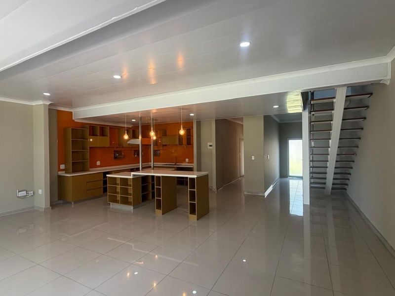 Spacious open-plan living area featuring a modern kitchen with built-in cabinetry, a central island, and a staircase leading to the upper level.
