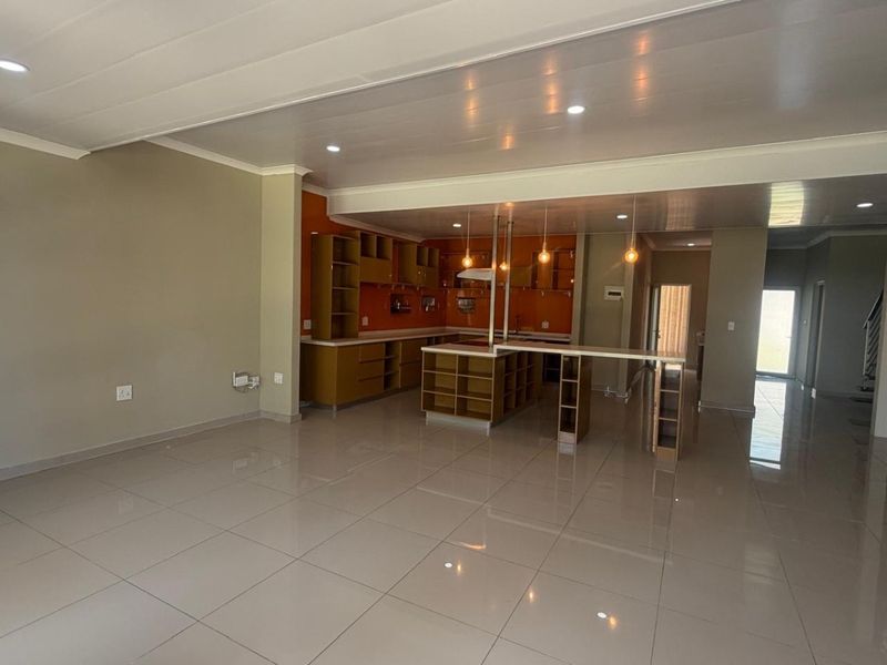 Spacious open-plan living and kitchen area featuring modern porcelain tile flooring, built-in cabinetry, and a functional kitchen island with a breakfast bar.