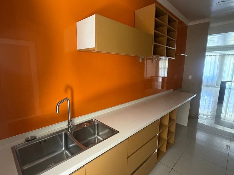 A clean and functional scullery featuring a double stainless steel sink, ample built-in cabinetry, open shelving, and a vibrant orange glass splashback.