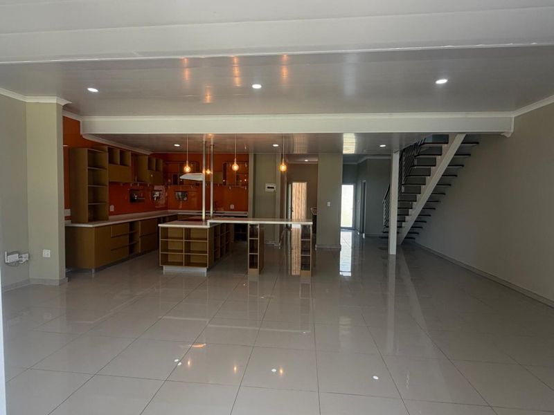 Spacious open-plan living area featuring a modern kitchen with built-in cabinetry, a central island, and a staircase leading to the upper level.