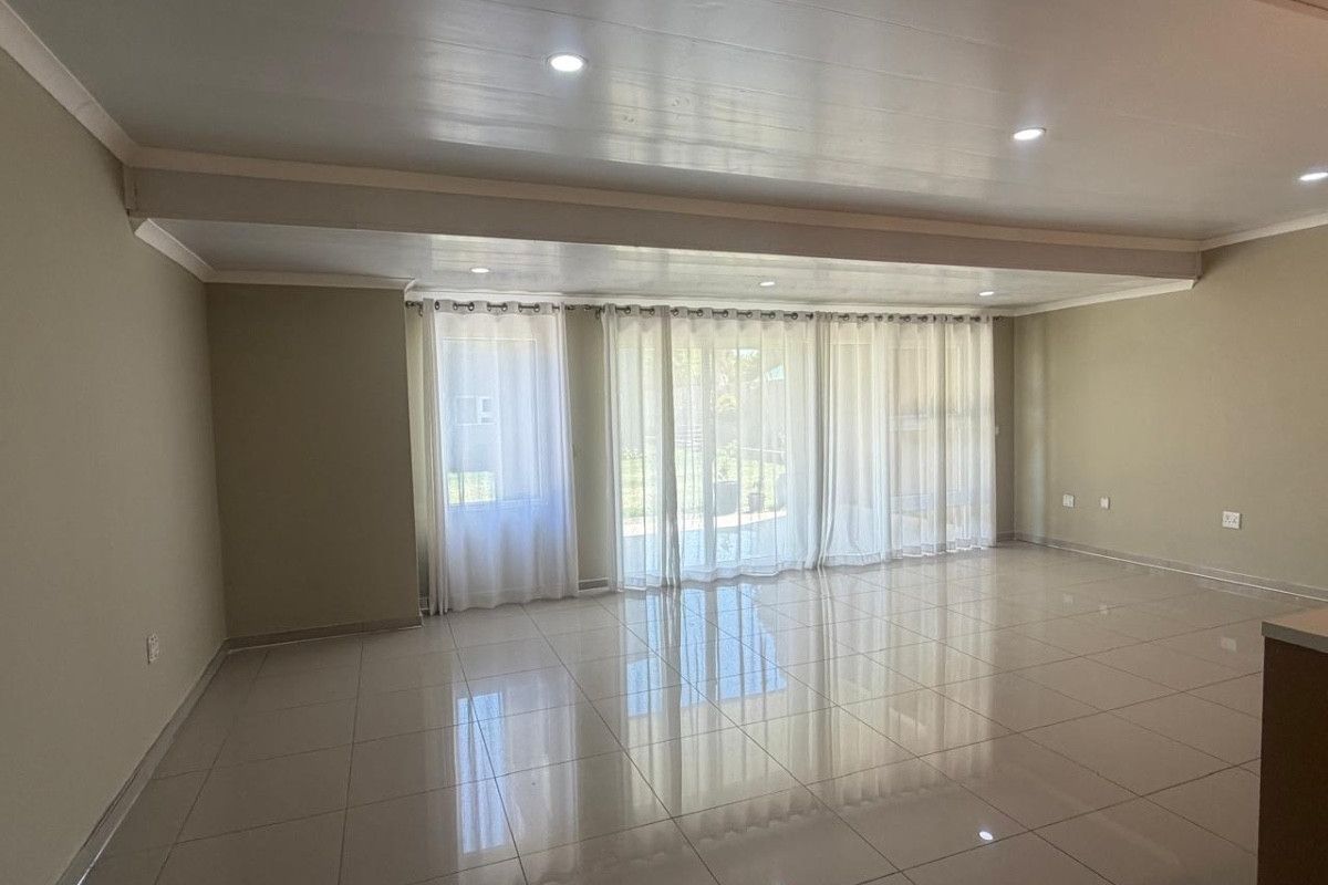 Spacious, light-filled living area featuring polished tiled flooring, recessed downlighting, and large sliding glass doors providing access to the exterior.