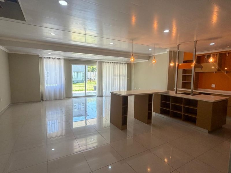 Spacious open-plan living and kitchen area featuring modern tiled flooring, a large kitchen island with built-in cabinetry, and sliding glass doors leading to the garden.