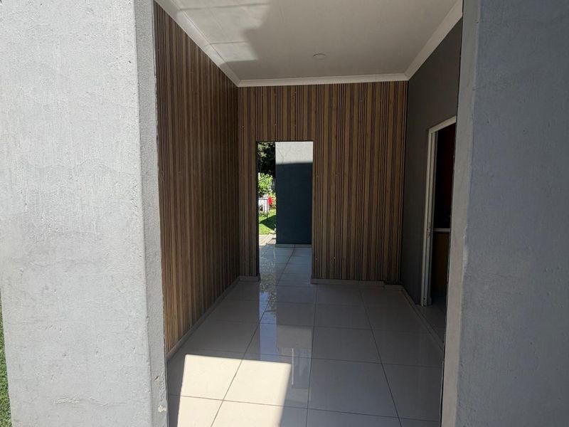 A covered outdoor patio area featuring modern tiled flooring and decorative wood-look wall paneling, providing a clean transition to the rear garden.