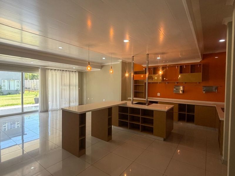 Spacious open-plan kitchen and living area featuring modern cabinetry, a central island with stone countertops, and large sliding doors leading to the garden.