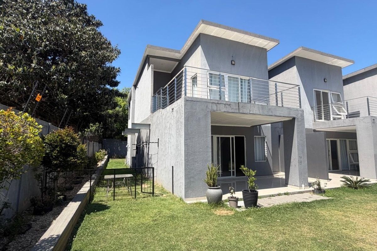 Rear view of a modern two-story townhouse featuring a private balcony, ground-floor patio, and a well-maintained garden area.