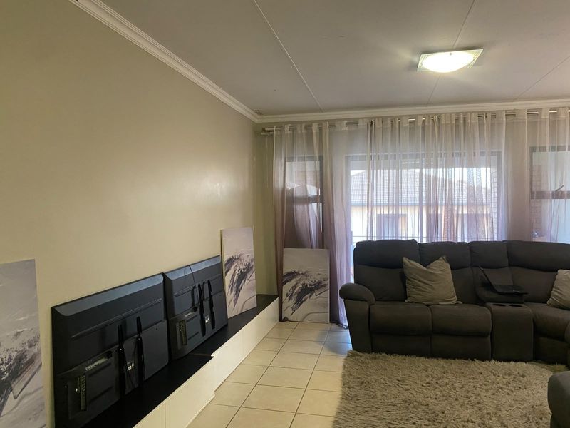 A living room featuring tiled flooring, built-in cabinetry, and a sliding glass door with sheer curtains, offering a functional and neutral living space.
