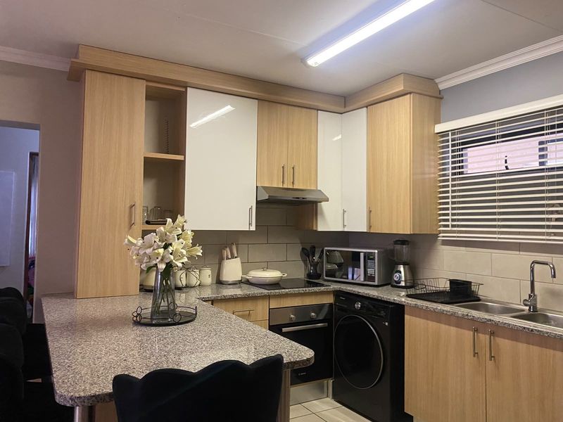 Modern kitchen featuring light wood cabinetry, granite countertops, integrated oven, hob, and extractor fan with a functional breakfast bar layout.