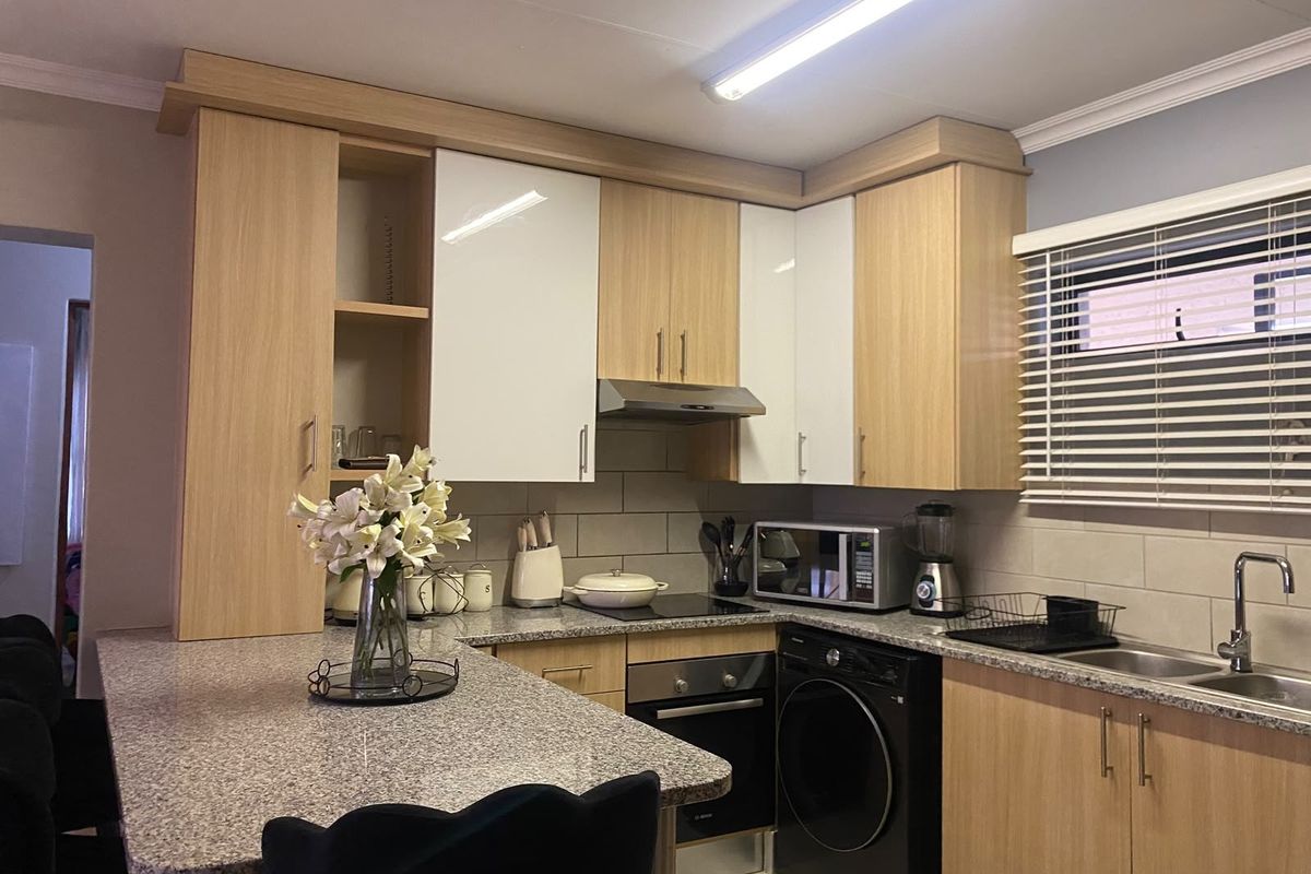 Modern kitchen featuring light wood cabinetry, granite countertops, integrated oven, hob, and extractor fan with a functional breakfast bar layout.