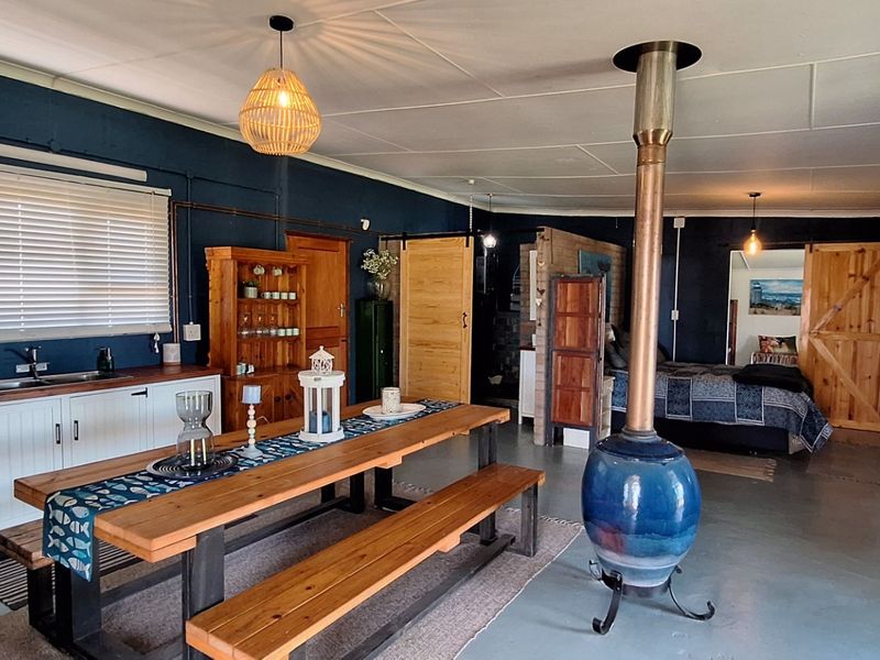 Spacious open-plan living area featuring a functional kitchen, dining space, and a central fireplace, with dark blue walls and polished concrete flooring.