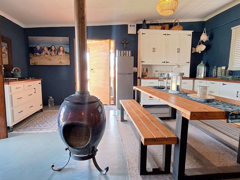 An open-plan kitchen and dining area featuring a central freestanding fireplace, white cabinetry with timber countertops, and direct access to the exterior.