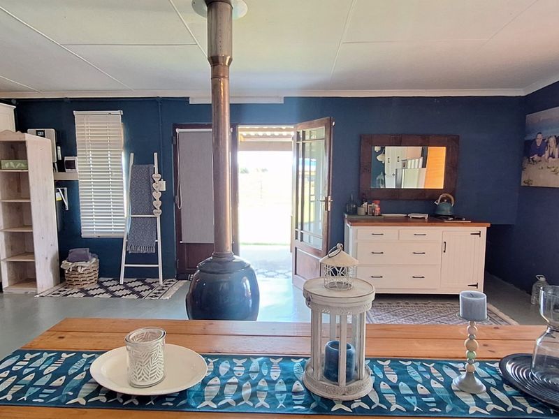 A living area featuring a central freestanding fireplace, painted concrete floors, and direct access to an outdoor patio through a timber door.