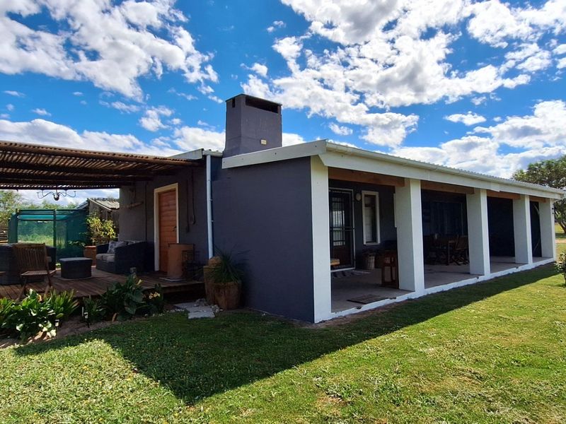 Rear view of the property featuring a covered patio with timber decking, pergola structure, and a prominent masonry chimney set within a landscaped garden.