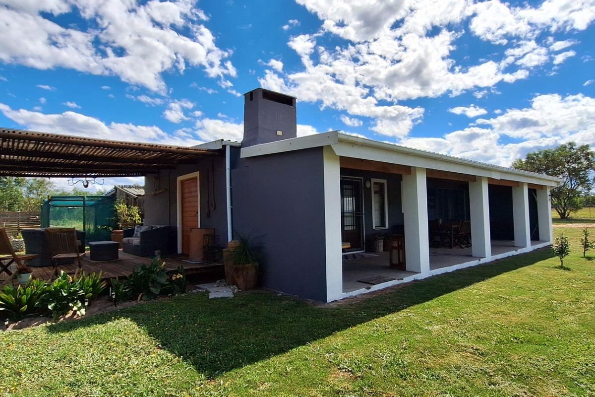 Rear view of the property featuring a covered patio with timber decking, pergola structure, and a prominent masonry chimney set within a landscaped garden.