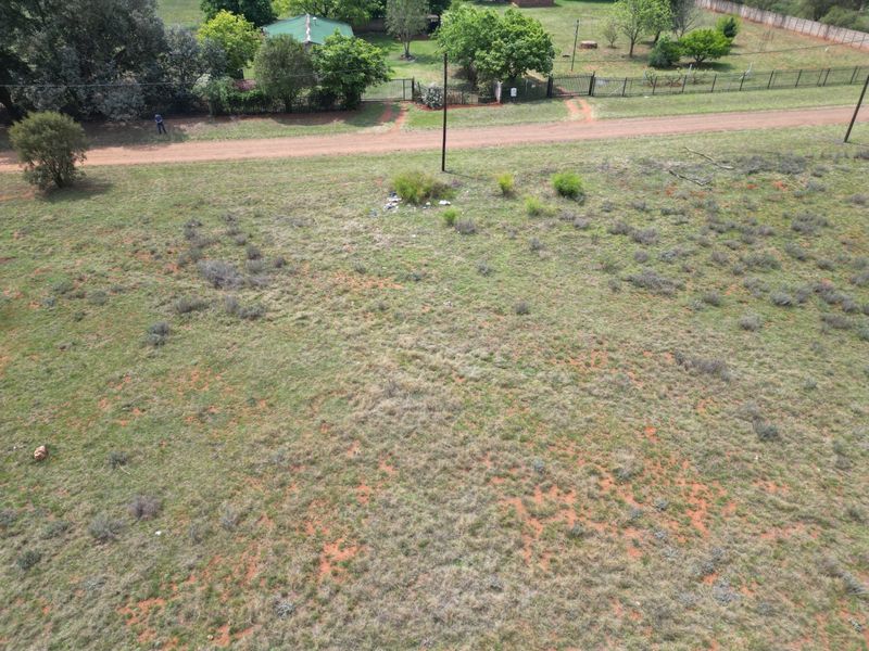 An aerial view of a vacant residential plot featuring natural grass cover, perimeter fencing, and a utility pole.