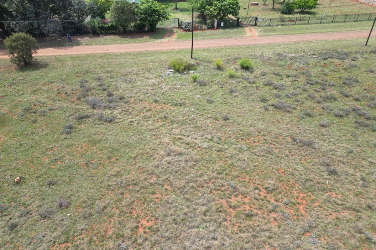 An aerial view of a vacant residential plot featuring natural grass cover, perimeter fencing, and a utility pole.