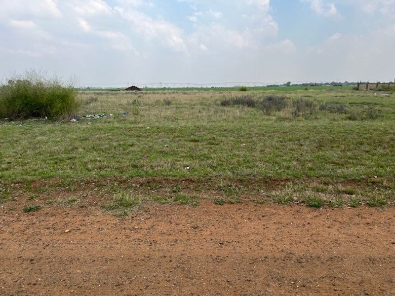 A view of a vacant residential plot of land featuring open grass and dirt terrain.