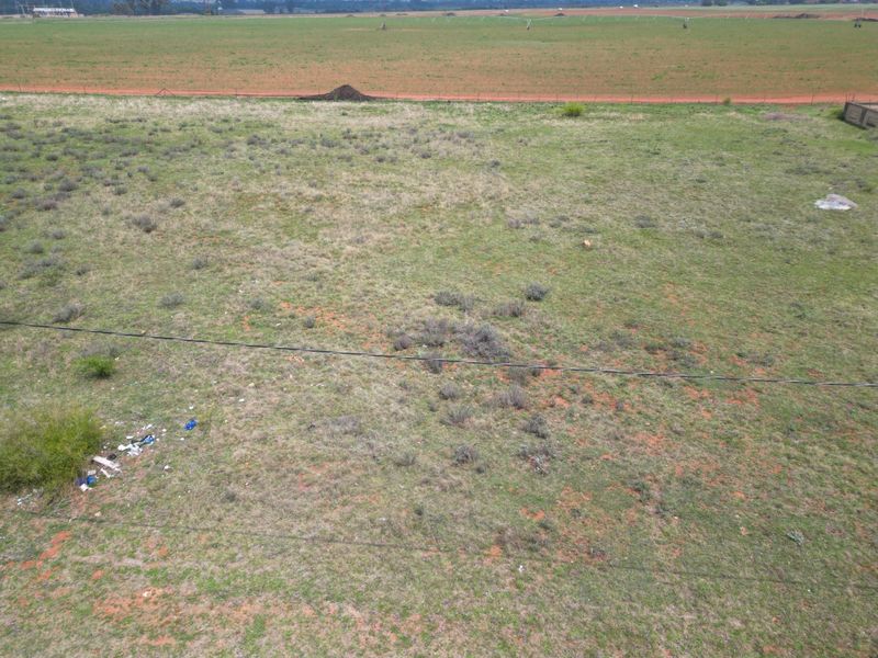 An aerial view of a vacant residential plot featuring natural grass cover, perimeter fencing, and overhead power lines.