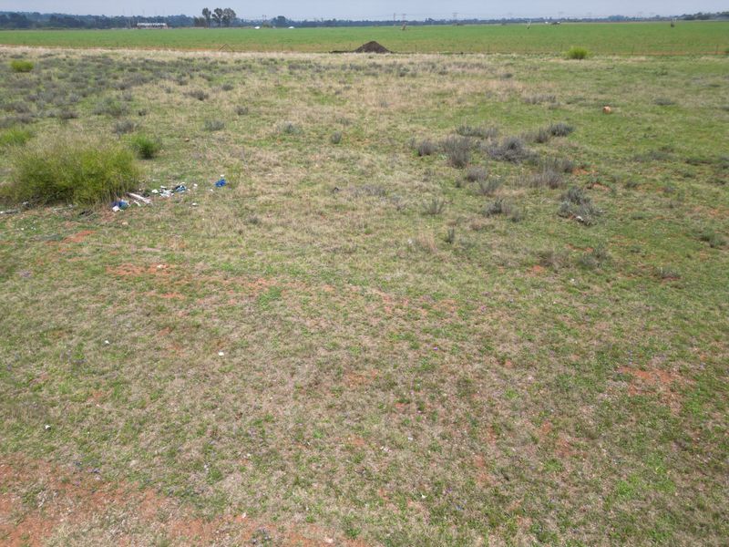 An expansive, undeveloped residential plot featuring natural grass cover and perimeter wire fencing, offering a clear view of the surrounding landscape.