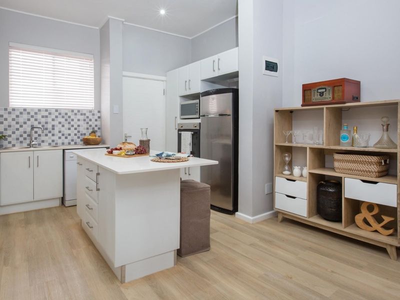Modern kitchen featuring a central island, white cabinetry, mosaic tile backsplash, built-in appliances, and light wood-look laminate flooring.
