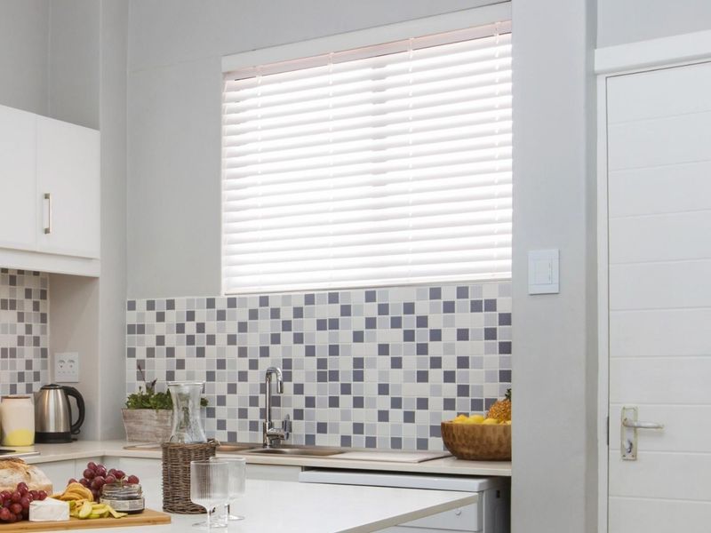 A clean, modern kitchen featuring white cabinetry, a mosaic tile backsplash, and a functional sink area with integrated hob.