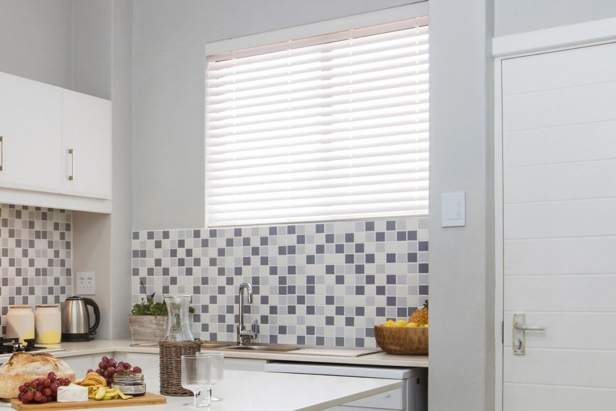 A clean, modern kitchen featuring white cabinetry, a mosaic tile backsplash, and a functional sink area with integrated hob.