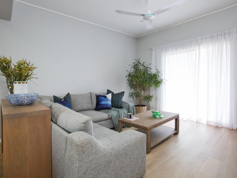 A bright and well-maintained living room featuring light laminate flooring, a ceiling fan, and a sliding glass door providing access to the outdoors.