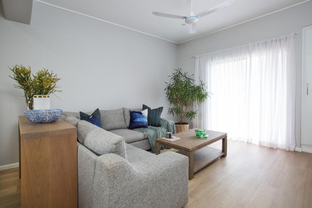 A bright and well-maintained living room featuring light laminate flooring, a ceiling fan, and a sliding glass door providing access to the outdoors.
